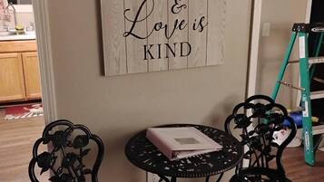 A room with a wall-mounted sign stating 'Love is patient & Love is kind,' a small round table with chairs, and a ladder in the background.