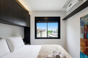 A hotel room with a bed, a window with a city view, and a painting on the wall. - Comfort in Condo With Pool and Garage Rpf0307 (Porto Alegre)