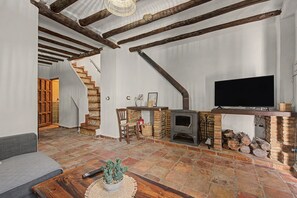 A rustic living room with exposed wooden beams, a fireplace, a television, and a staircase leading to another room.