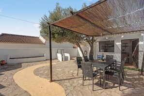 Un patio con suelo de piedra, una mesa con sillas y una pérgola que da sombra.