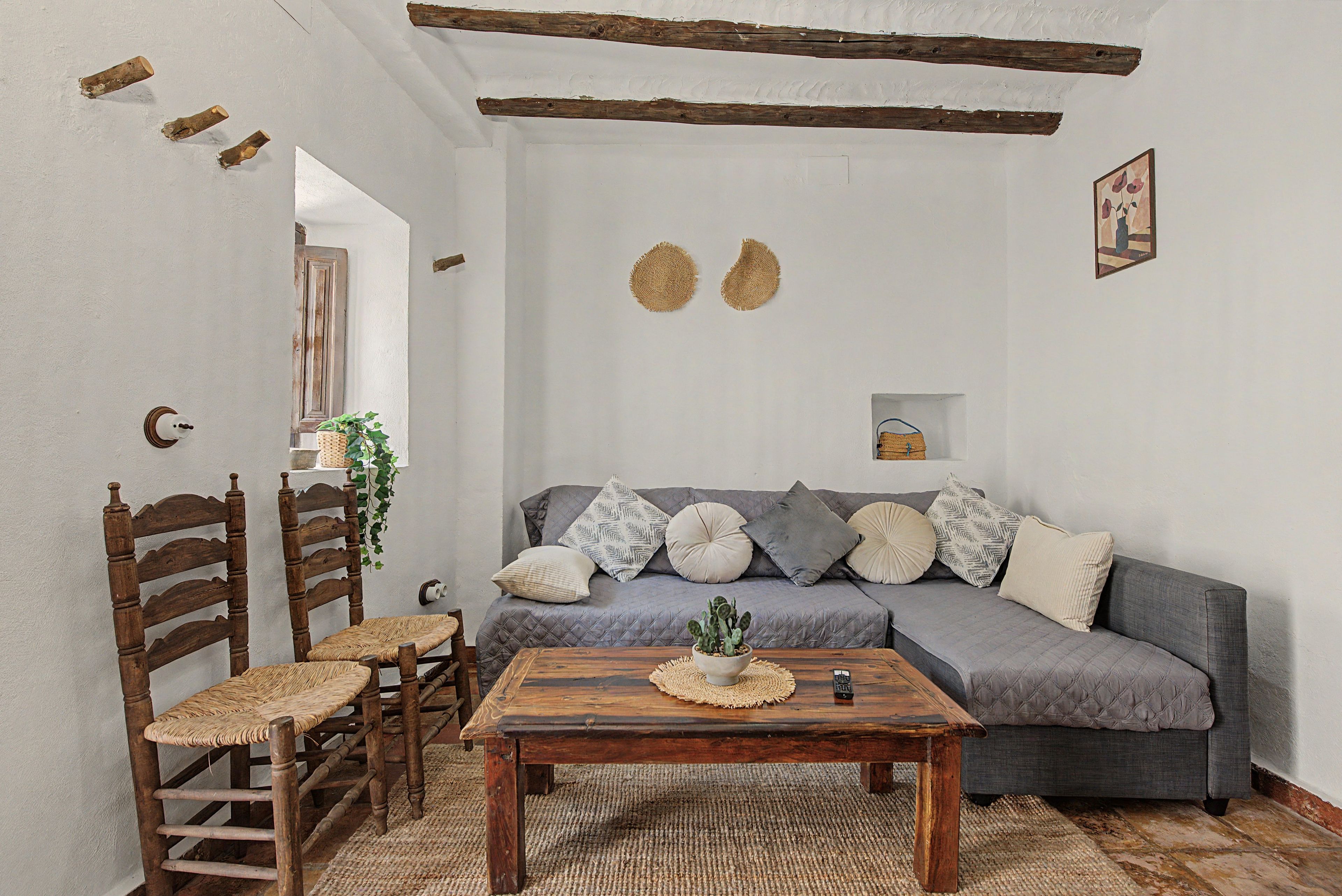 A cozy living room with a grey sofa, wooden chairs, a coffee table, and a hanging plant.