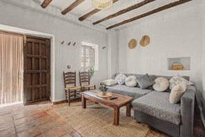 A cozy living room with a wooden door, a sofa with cushions, a coffee table, and a woven rug.