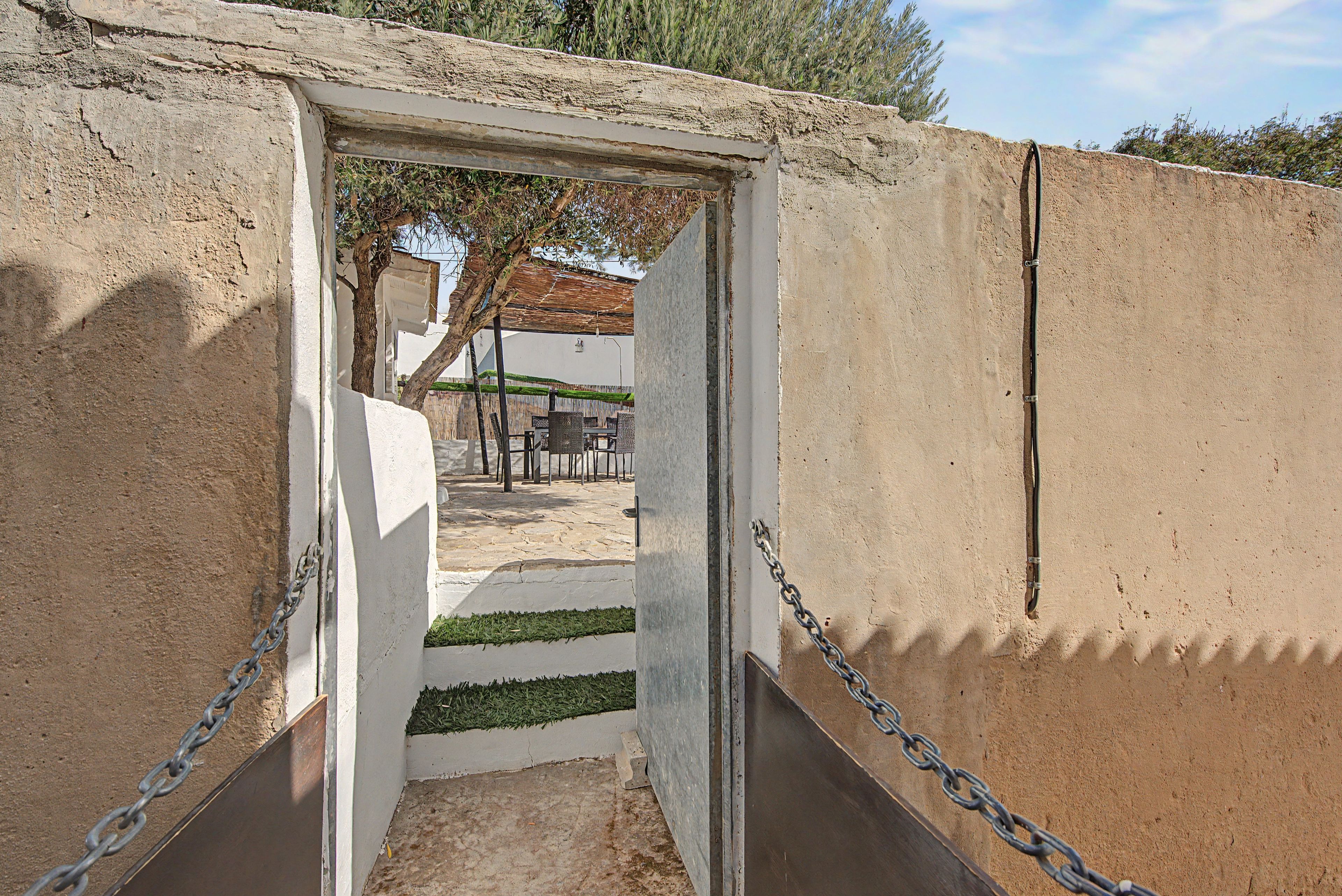 Una puerta que da a un espacio al aire libre con una mesa y sillas, rodeado por una cerca de malla.