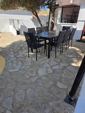 Une terrasse extérieure avec un sol en pierre, une table en bois et des chaises en osier noir.