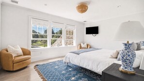 Ein Schlafzimmer mit einem Bett, einem Sessel, einem Fernseher und einem Fenster mit Blick auf ein Haus.
