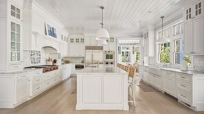 A spacious kitchen with white cabinetry, a large island, and a dining area with chairs. - Luxury Southold escape featuring a private pool, movie theater, gym, and... (Southold)