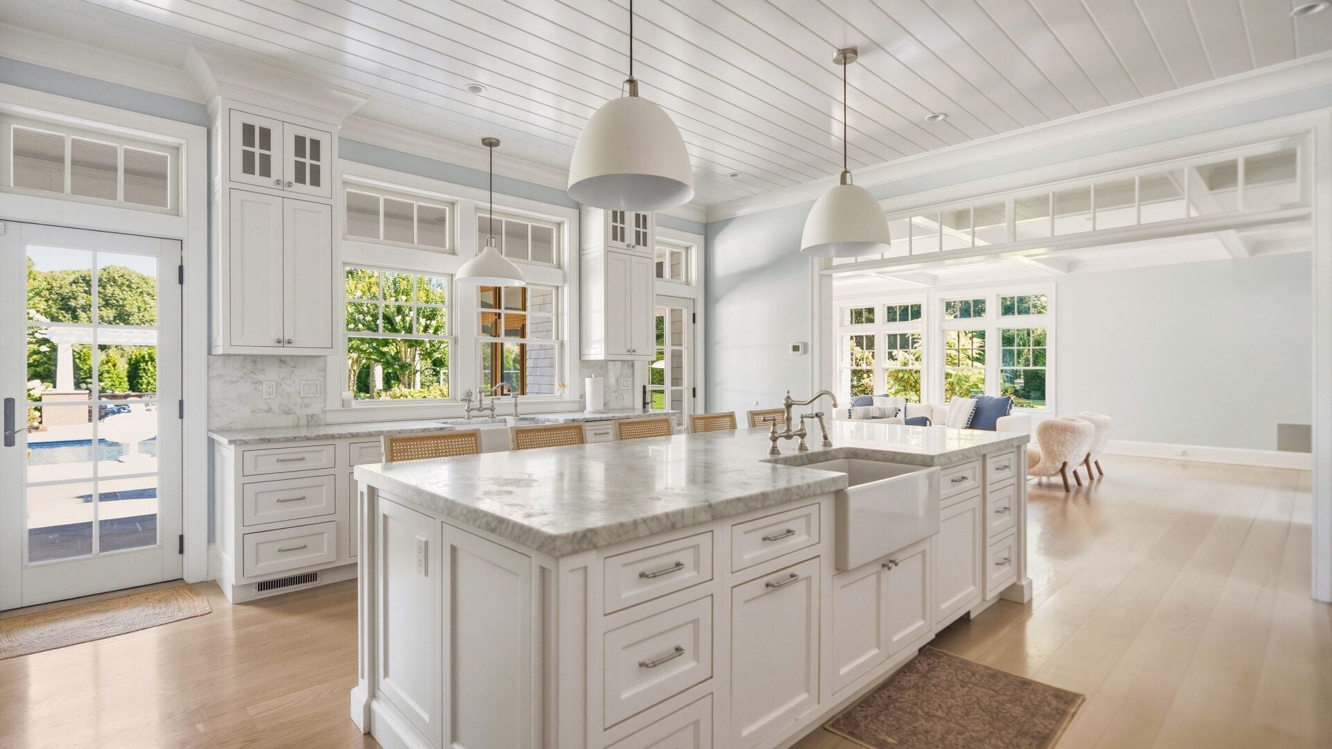 A spacious kitchen with white cabinetry, a large island, pendant lighting, and a view of a pool and greenery outside.