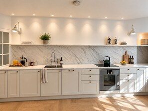 A modern kitchen with white cabinetry, a marble backsplash, and built-in appliances. - Gladstone House (London)