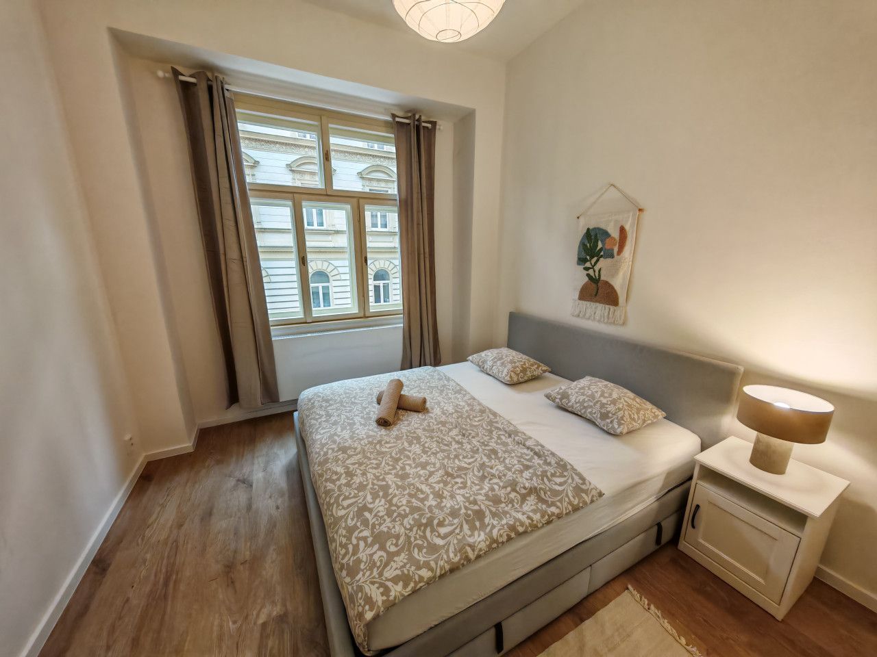 Une chambre à coucher avec un grand lit, une table de chevet avec une lampe et une fenêtre avec des rideaux.