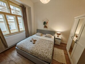 A bedroom with a bed, bedside tables, a wardrobe, and a window with curtains. - Modern 1BR in trendy Žižkov (Praha 3)