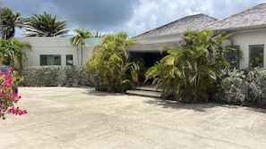 A modern building with a concrete driveway, surrounded by tropical plants and a clear sky. - Daniel Bay - Modern 6-bedroom beachfront house in Willoughby Bay (St Paul)