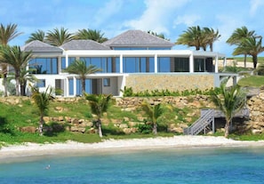 A modern beachfront property with a large house, a stone retaining wall, and palm trees. - Daniel Bay - Modern 6-bedroom beachfront house in Willoughby Bay (St Paul)