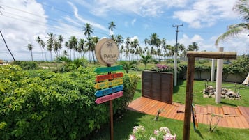 Un cartel con indicaciones hacia varias instalaciones, como piscina, playa y parque, con un paisaje tropical de fondo.