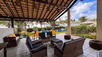 A covered outdoor seating area with wicker furniture and a pool in the background.