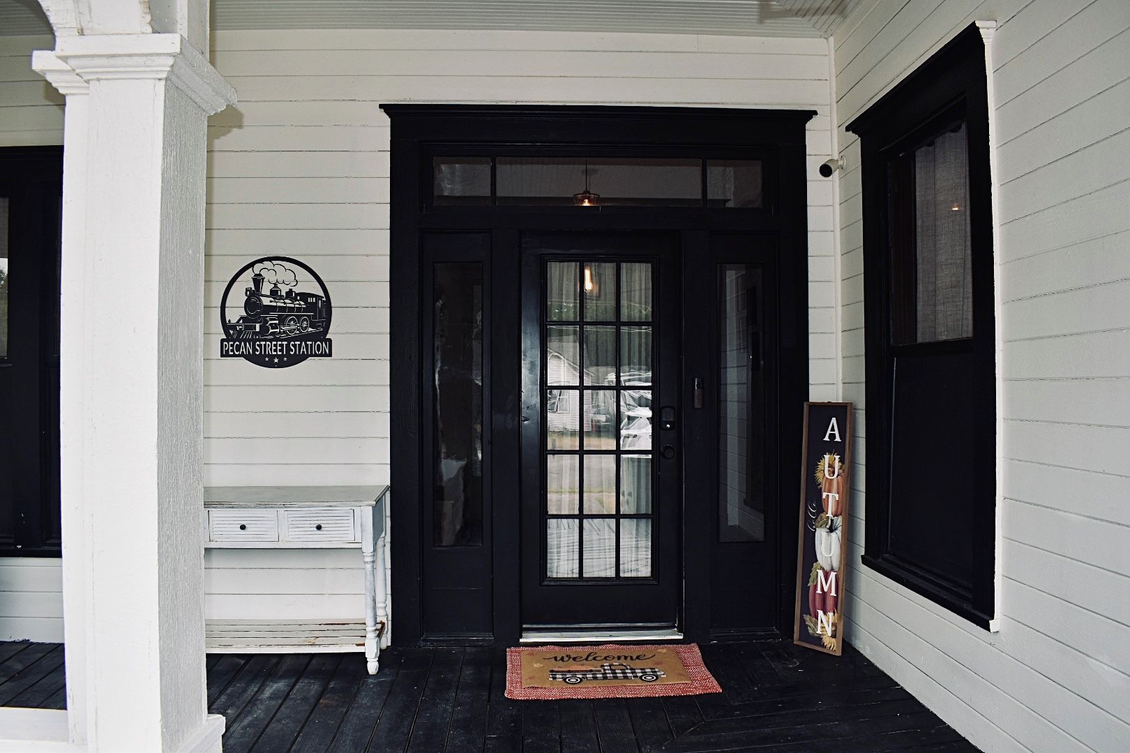 A black door with a glass panel, a welcome mat, and a sign reading 'PECAN STREET STATION' on the wall.