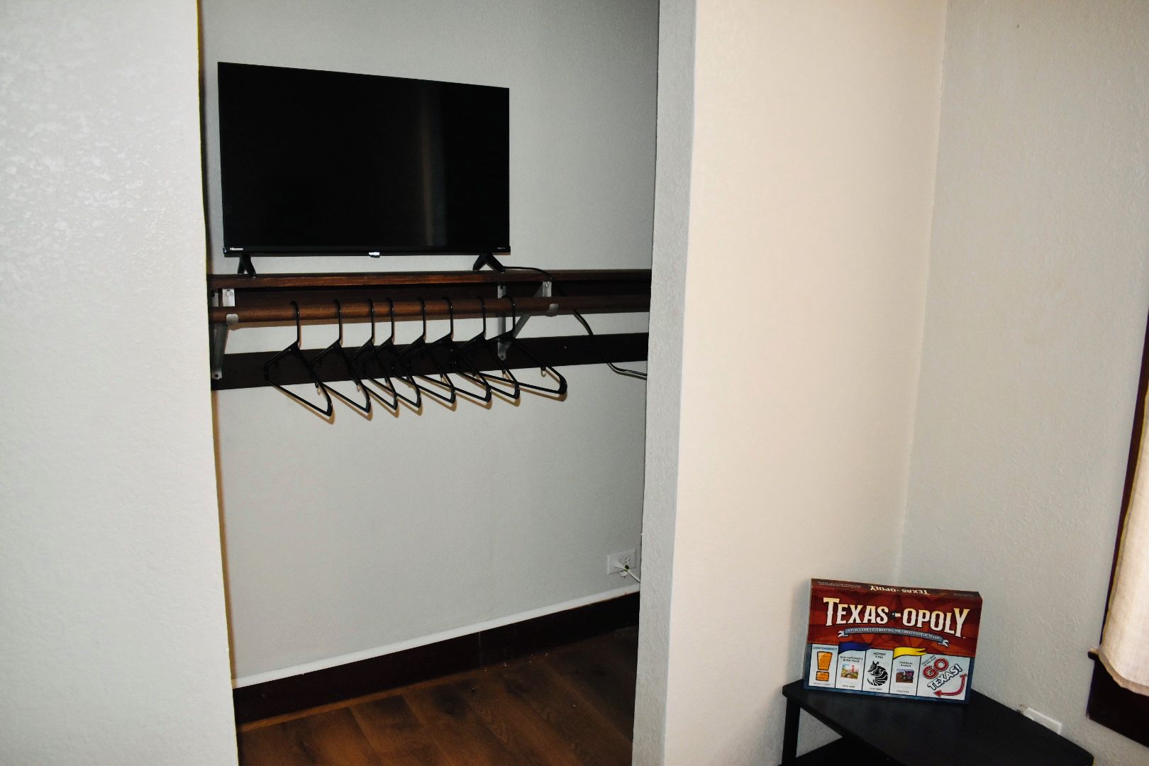 A room with a mounted television, a coat rack, and a Texas-Opoly game box on a table.