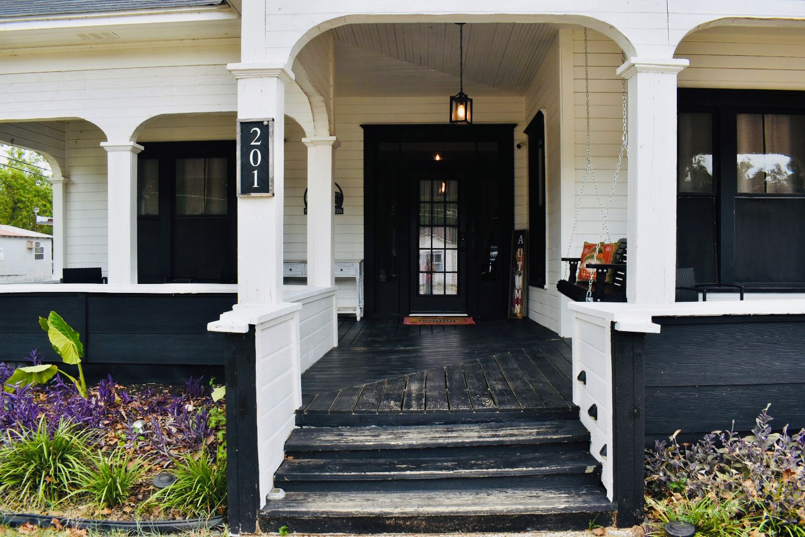 A house with a black front porch, white columns, and a number sign indicating the address.