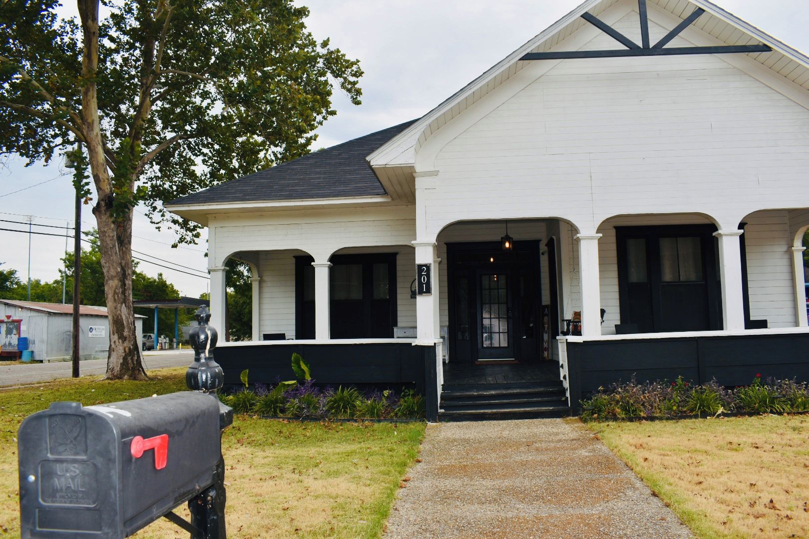 A white building with a black front door, a mailbox, and a tree in the background.