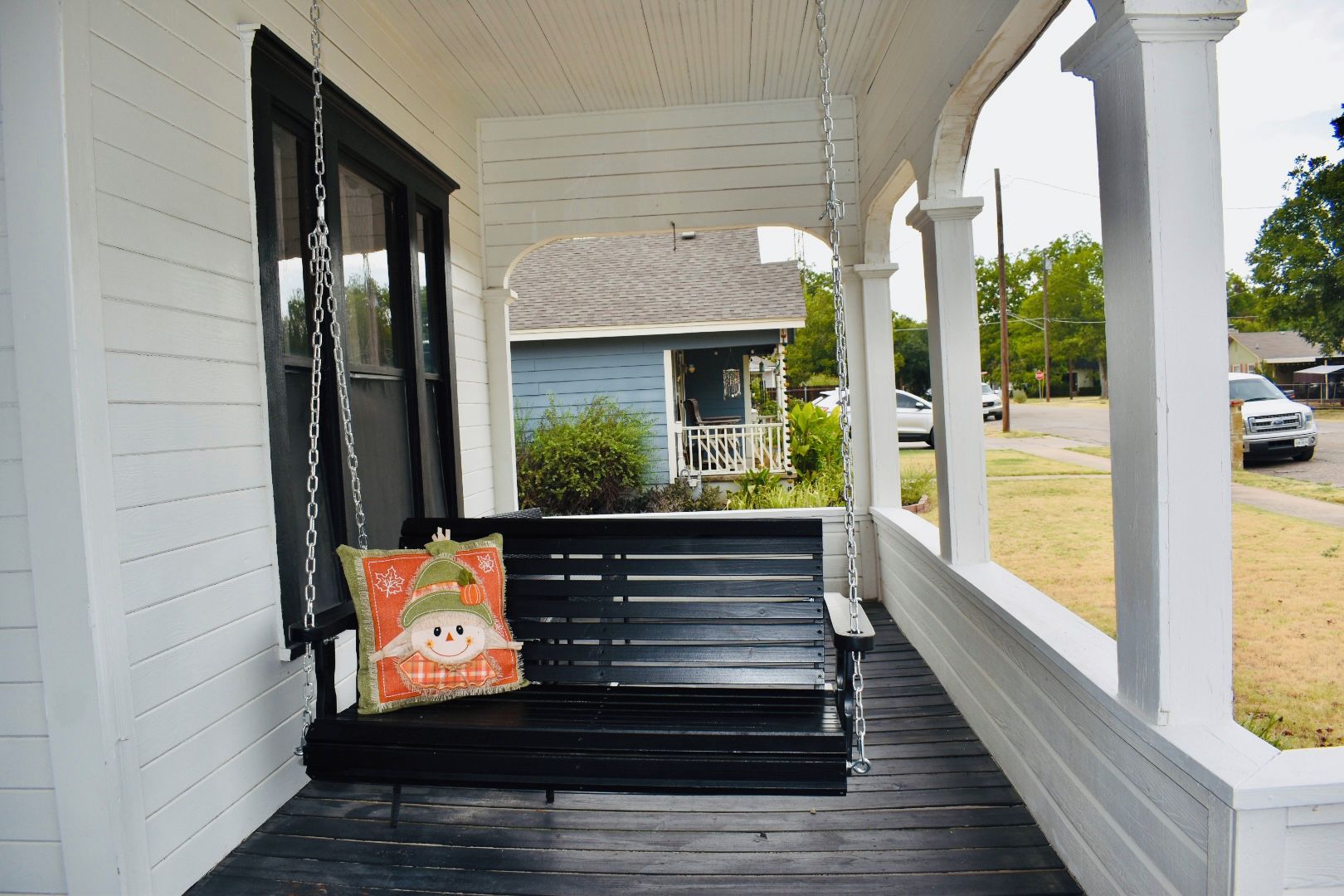A porch with a black swing and a cushion with a pumpkin design.