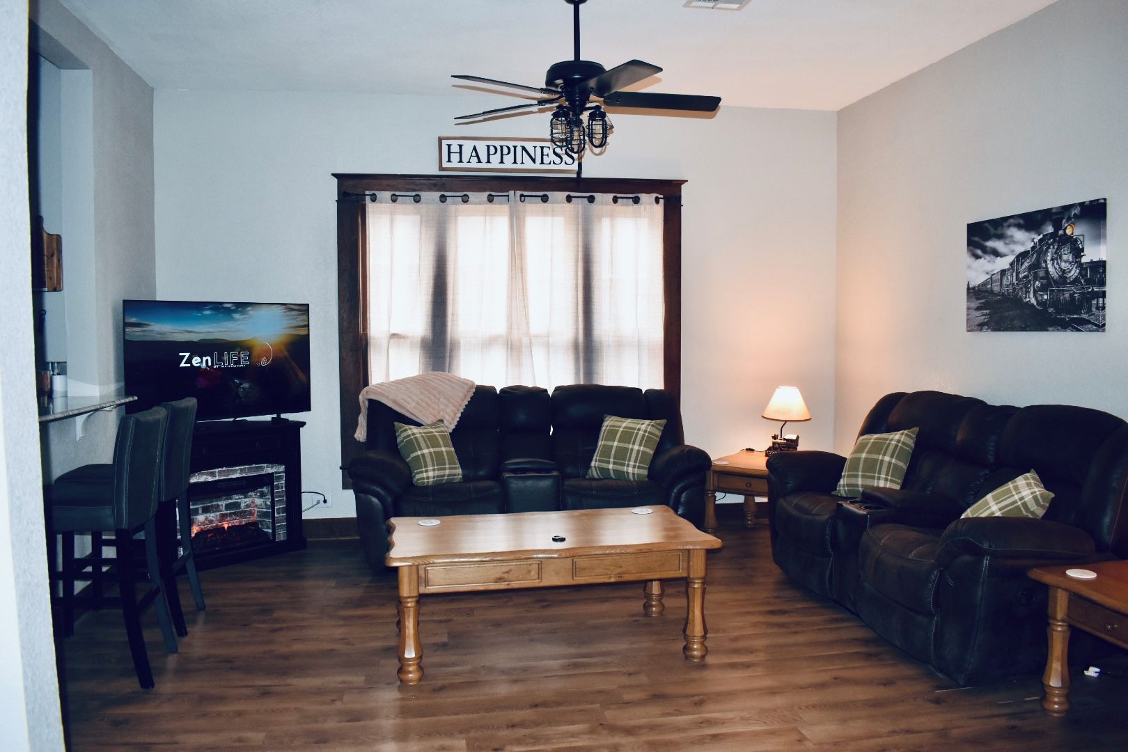 Una sala de estar con televisor, dos sofás, una mesa de centro y un ventilador de techo.