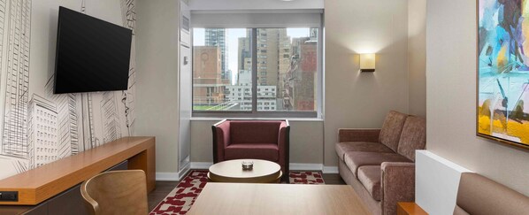 A modern living room with a flat-screen TV, a round coffee table, a red armchair, a brown sofa, and a large window with a city view.