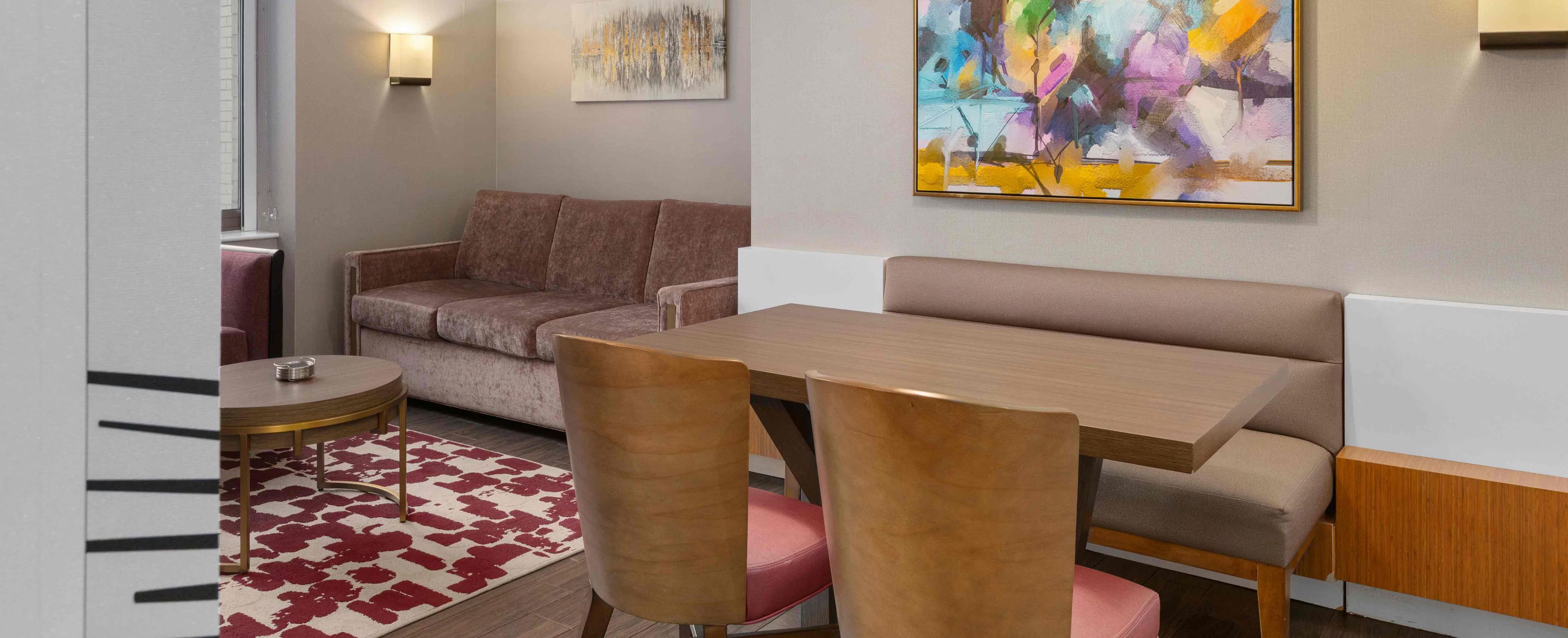 A compact living space with a sofa, a dining table with chairs, a small round table, and a colorful abstract painting on the wall.