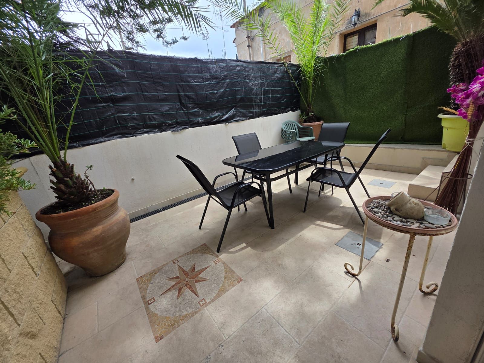 An outdoor patio with a table and chairs, a potted plant, and a decorative tile floor.