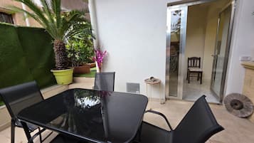 Un patio con un tavolo e sedie in vetro, circondato da piante in vaso e un piccolo tavolino rotondo.