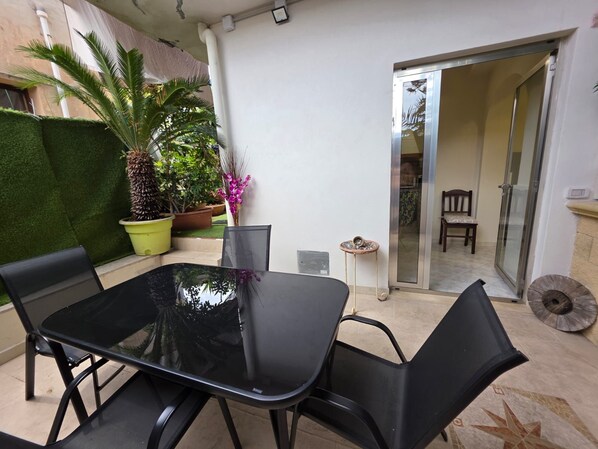 Eine Terrasse mit einem Glastisch und Stühlen, umgeben von Topfpflanzen und einem kleinen runden Tisch.
