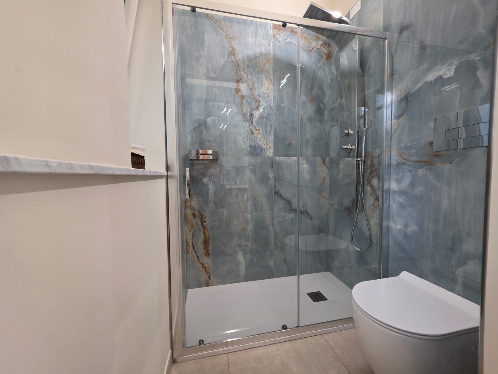 Ein modernes Badezimmer mit einer Duschkabine aus Glas, einer weißen Toilette und einer Marmor-Spritzschutzwand.