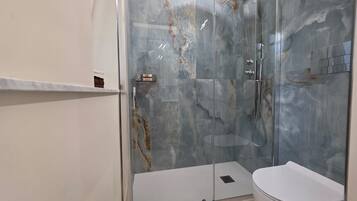 Ein modernes Badezimmer mit einer Duschkabine aus Glas, einer weißen Toilette und einer Marmor-Spritzschutzwand.