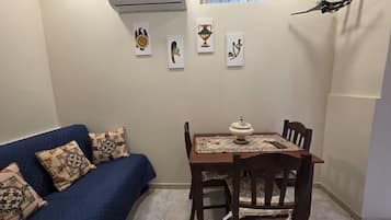 A small room with a blue sofa, a wooden dining table with chairs, and a decorative wall with framed artwork.