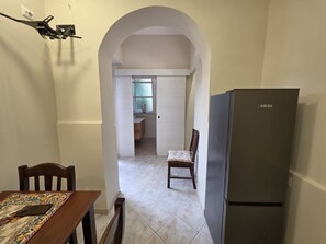 Eine Küche mit einem Kühlschrank, einem Esstisch mit Stühlen und einem Durchgang zu einem Badezimmer.