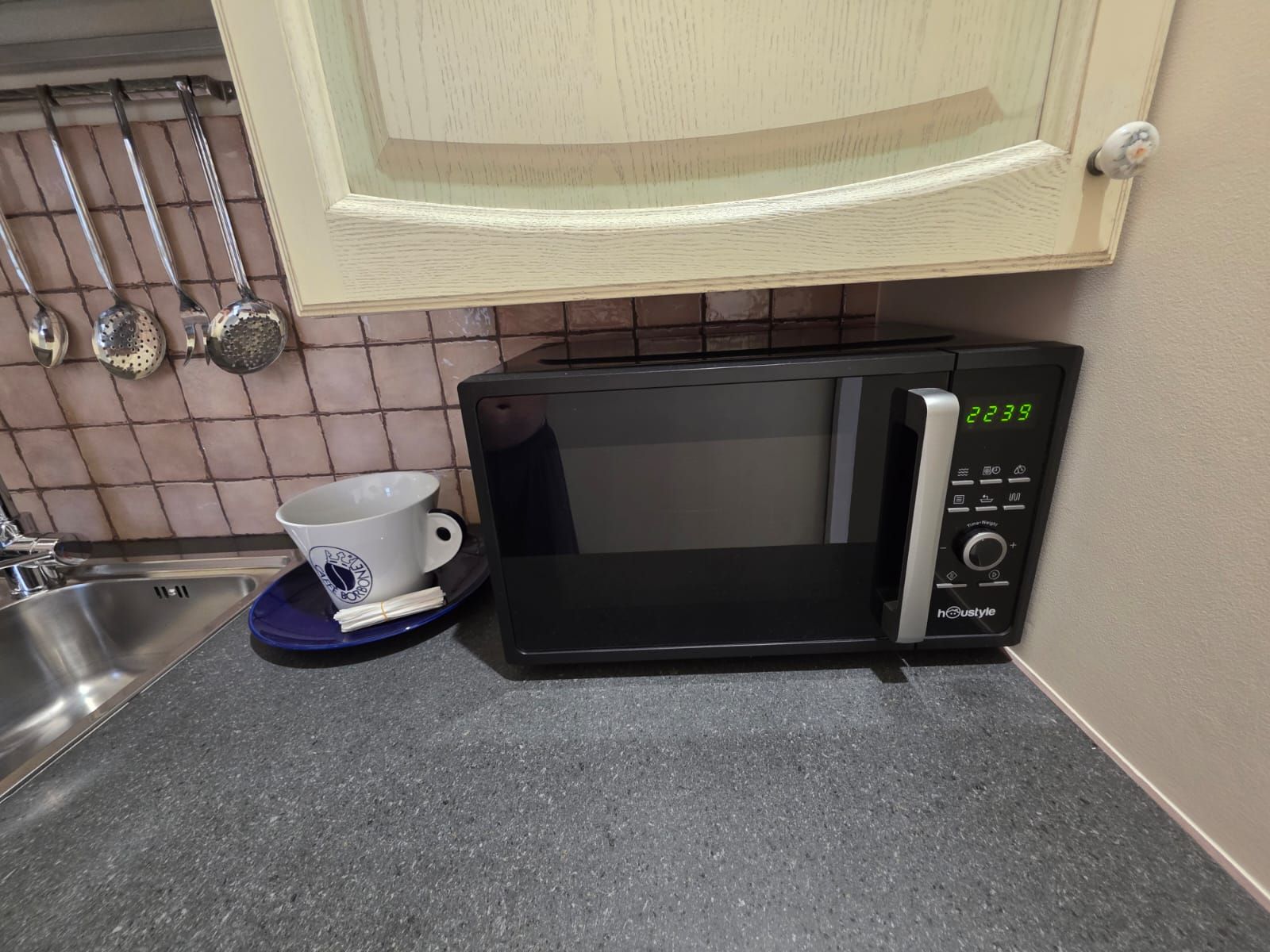 A kitchen with a microwave, a sink, and a cabinet above the microwave.