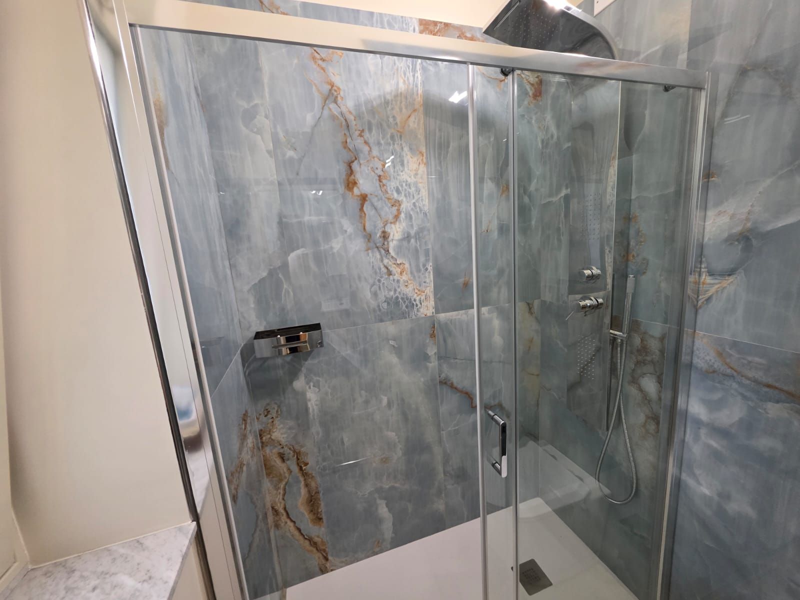 Un box doccia moderno con porta in vetro e interni alla parete dall'aspetto marmorizzato.