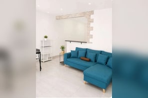 Ein modernes Wohnzimmer mit einem blauen Ecksofa, einem kleinen Beistelltisch mit einer Pflanze und einem weißen Regal.