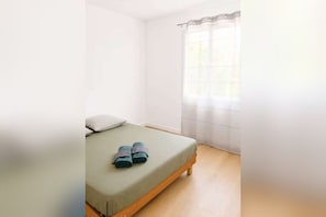 Ein Einzelbett mit einer grünen Matratze, einem Kopfkissen und zwei zusammengerollten Handtüchern.