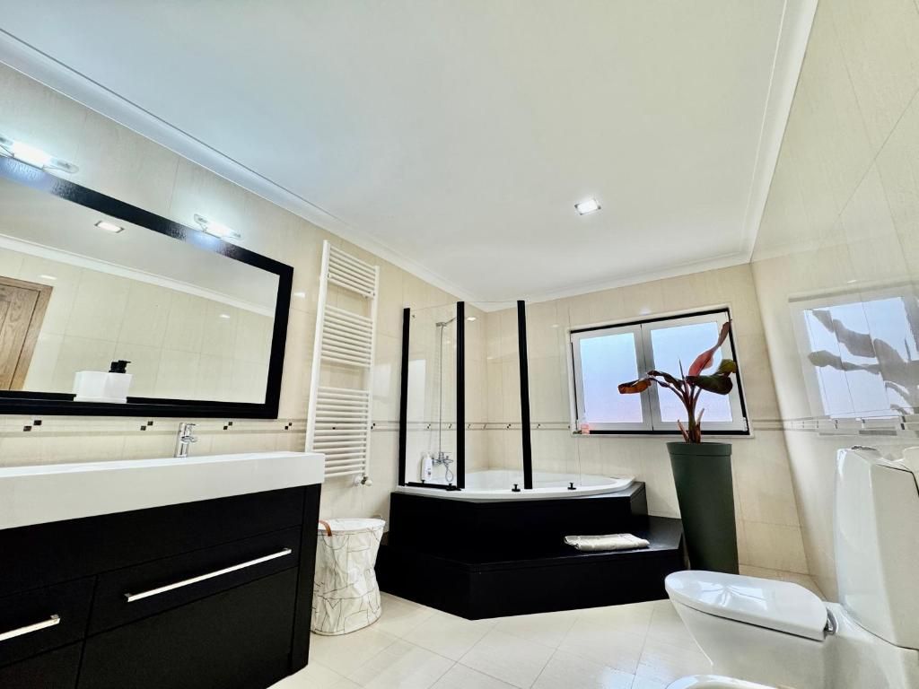 A modern bathroom with a large mirror, a bathtub, a toilet, and a sink.
