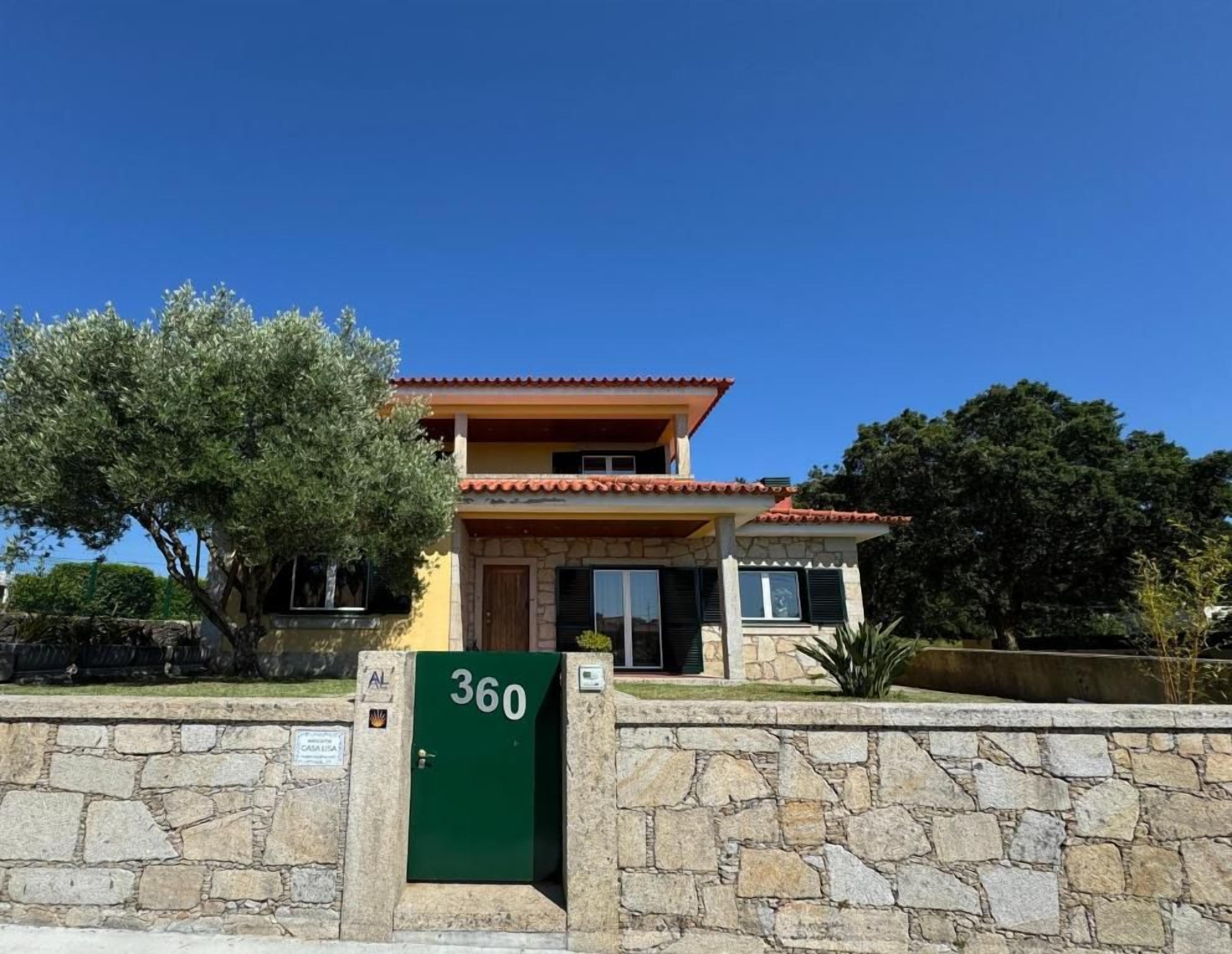 A two-story house with a stone wall in front, a green sign with the number 360, and a clear blue sky.