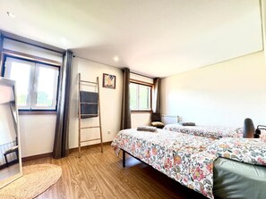 Une pièce avec un plancher en bois, deux lits avec une literie à motifs floraux, une échelle, un miroir et une fenêtre avec des rideaux.