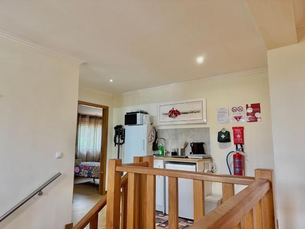 A hallway leading to a bedroom with a bed, a kitchen area with a microwave, and a fire extinguisher on the wall. - Etape Casa Lisa (Caminha)