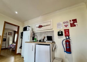 A compact kitchenette with a refrigerator, microwave, and coffee maker. A fire extinguisher is mounted on the wall. - Etape Casa Lisa (Caminha)