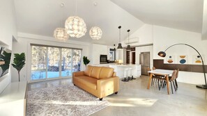 A spacious living room with a sofa, a dining area with a table and chairs, a kitchen with modern appliances, and a large window with a view of trees. - Luxury Cottage - Detox & Relaxation (Stone Mills)