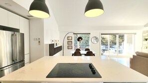 A modern kitchen with a central island, stainless steel appliances, pendant lighting, and a dining area with a view of the outdoors. - Luxury Cottage - Detox & Relaxation (Stone Mills)