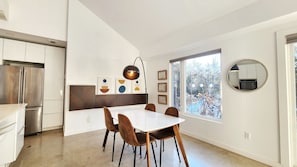 A modern kitchen with a built-in refrigerator, a dining area with a white table and brown chairs, and a large window with a view of trees. - Luxury Cottage - Detox & Relaxation (Stone Mills)