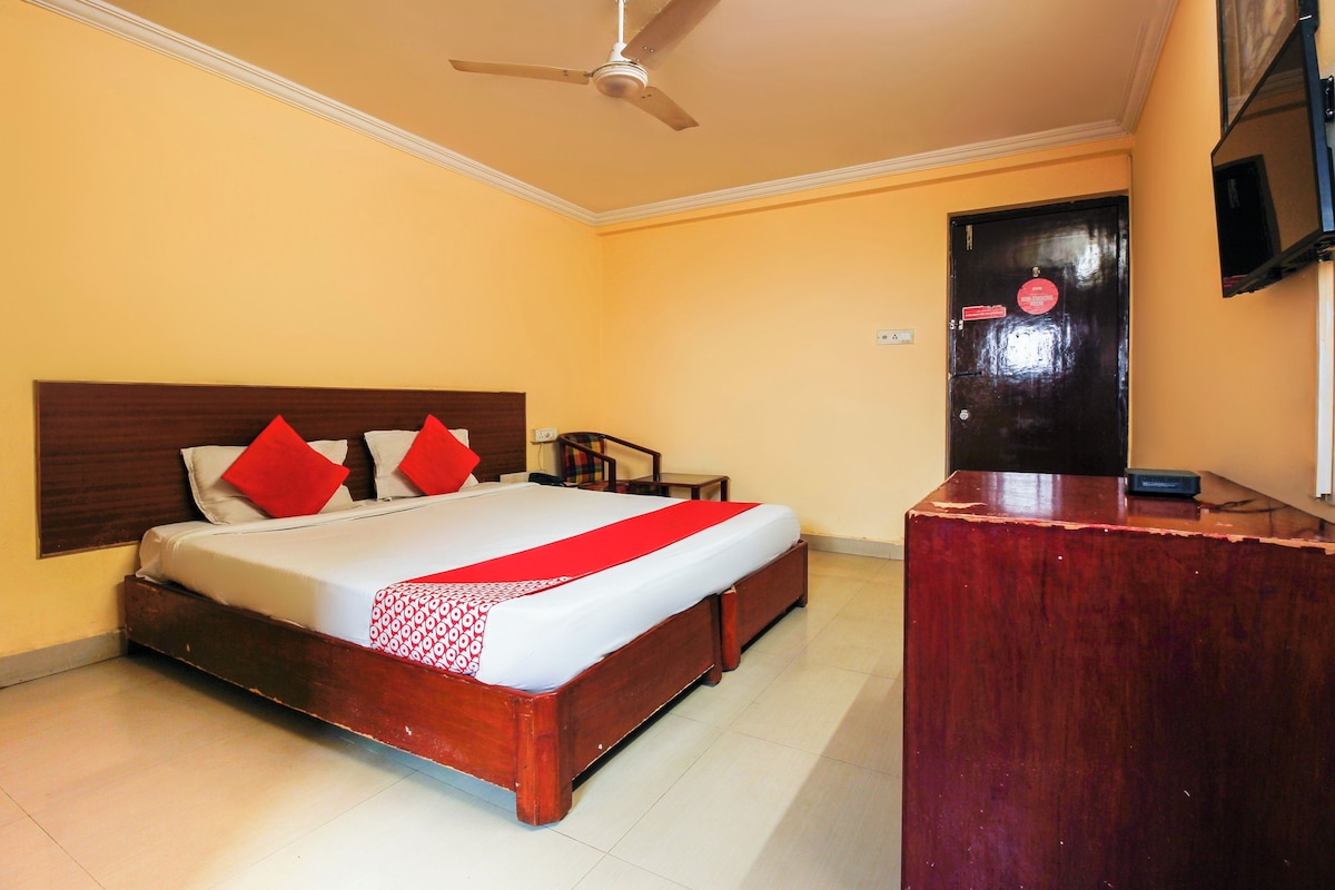 A hotel room with a bed, a desk, a chair, a ceiling fan, and a door with a sign.