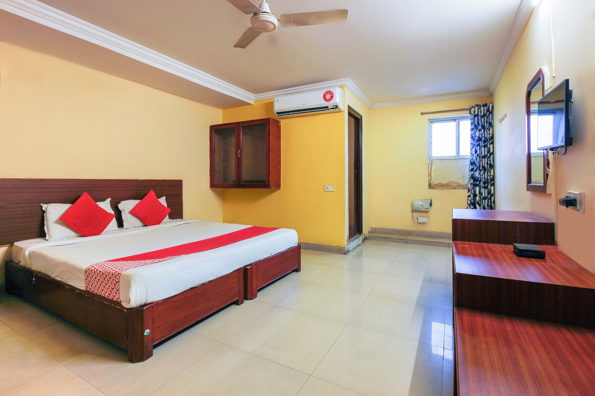 Una habitación de hotel con cama, escritorio, espejo, unidad de aire acondicionado y ventilador de techo.