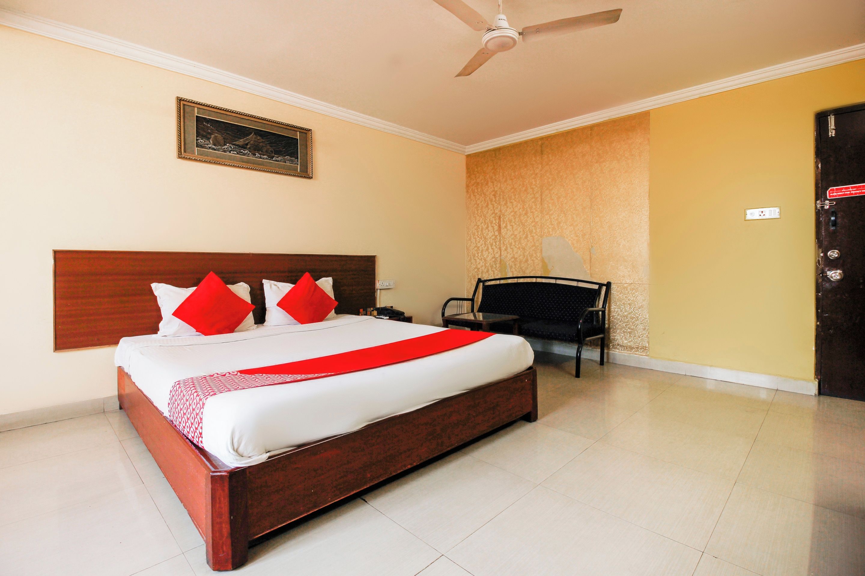Habitación de hotel con una cama grande, un ventilador de techo, una silla y una puerta.