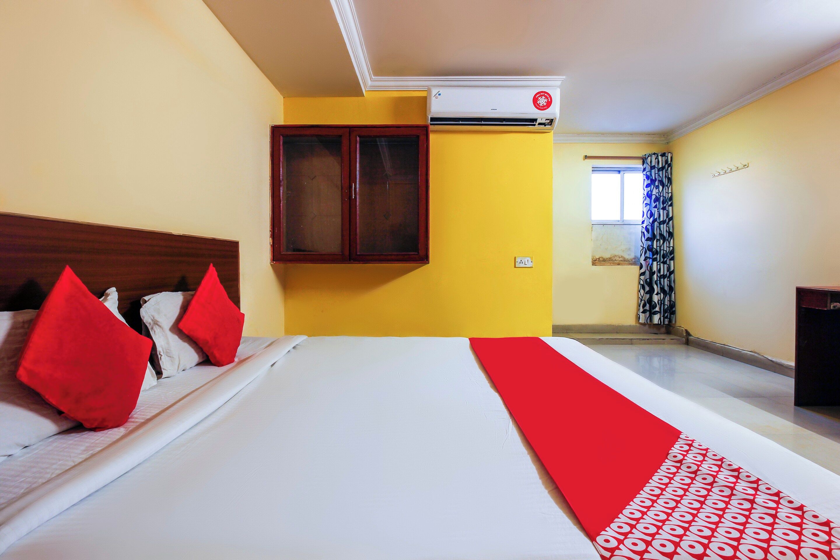 A hotel room with a bed, a window with curtains, an air conditioning unit, and a wall-mounted cabinet.
