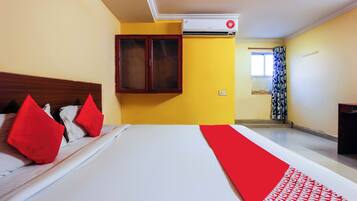 A hotel room with a bed, a window with curtains, an air conditioning unit, and a wall-mounted cabinet.
